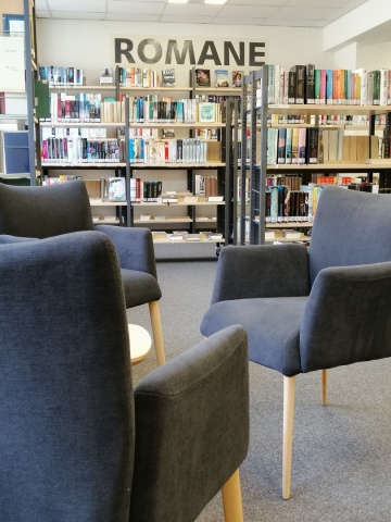 Das Bild zeigt die Romanabteilung der Bibliothek. Viele Regale mit Büchern und Sesseln zum ausruhen sind zu sehen.
